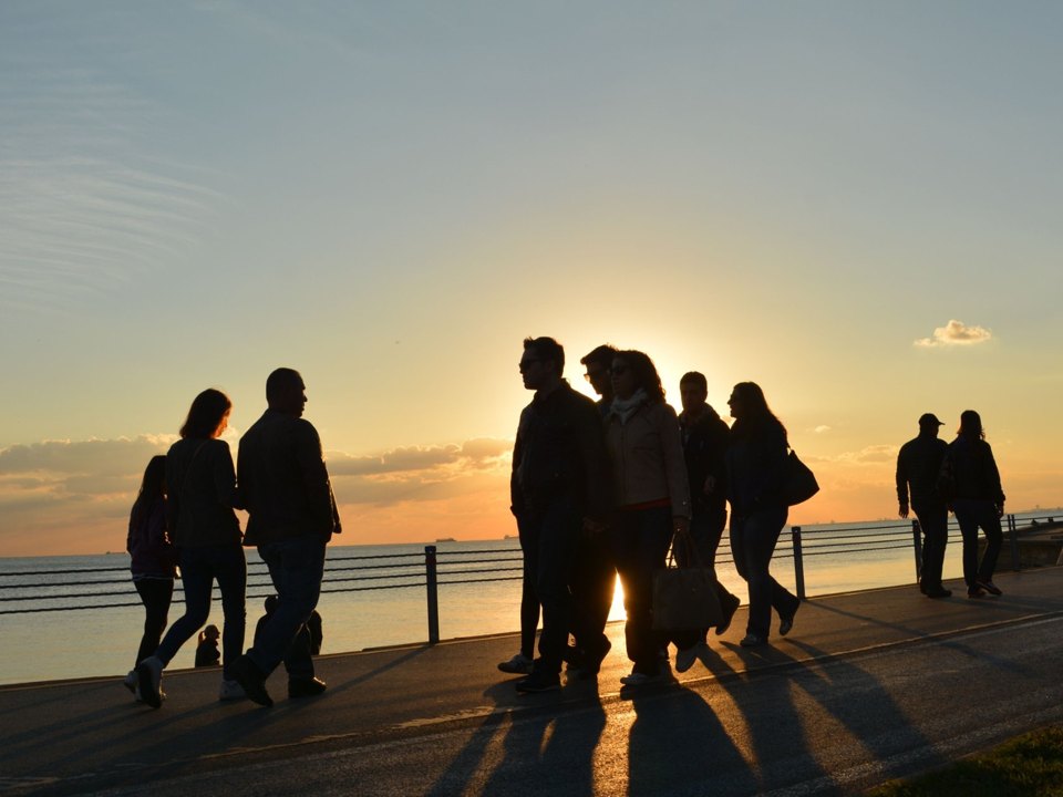 Folk som går tur langs vannet i solnedgang